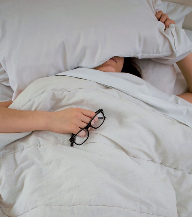 female in bed with white bedding and holding glasses